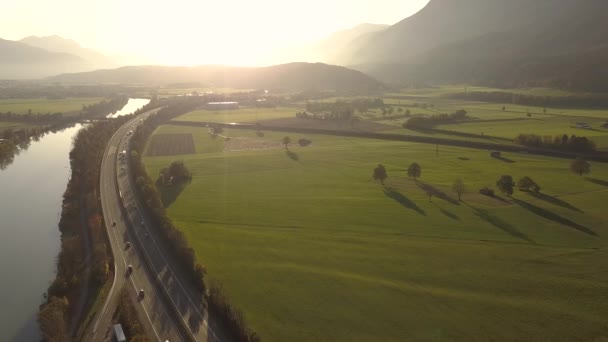 緑のフィールドとアルプスの山の間の農村部で高速移動交通と高速道路州間道路の空中ビュー — ストック動画