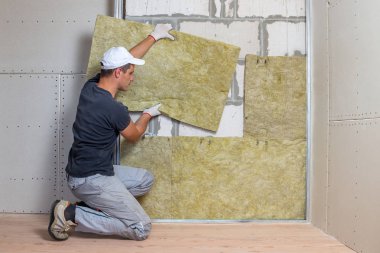 Bir oda duvarını mineral kaya yünleriyle yalıtan işçiler.