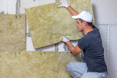 Bir oda duvarını mineral kaya yünleriyle yalıtan işçiler.
