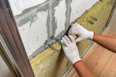 Bir oda duvarını mineral kaya yünleriyle yalıtan işçiler.