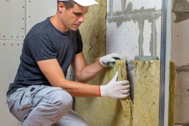 Bir oda duvarını mineral kaya yünleriyle yalıtan işçiler.