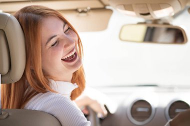 Genç kızıl saçlı kadın sürücü mutlu bir şekilde gülümsüyor..