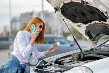 Kaputu patlamış, kırık bir arabanın yanında duran genç bir kadın konuşuyor.