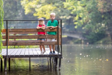 Göl kıyısında tahta güvertede duran iki kız ve erkek çocuk.