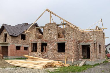 Yorumun altında ahşap çatı yapısı olan tamamlanmamış tuğla ev