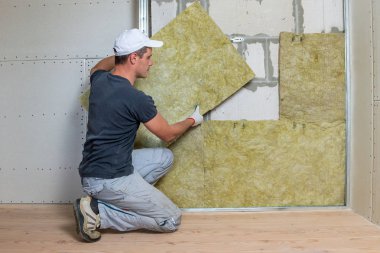 Bir oda duvarını mineral kaya yünleriyle yalıtan işçiler.