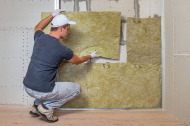 Bir oda duvarını mineral kaya yünleriyle yalıtan işçiler.