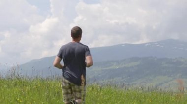 Genç bir turist yaz dağlarında yürüyüş yaparken elini kaldırıyor..