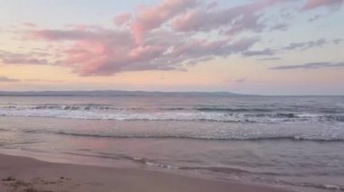 Mor günbatımı gökyüzü altında mavi su dalgaları olan bir deniz yüzeyinin havadan görünüşü.