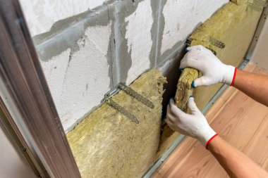 Bir oda duvarını mineral kaya yünleriyle yalıtan işçiler.