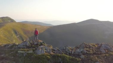 Kayalık dağın tepesinde duran yürüyüşçü muhteşem manzaranın tadını çıkarıyor. Dağcı dağlarda güneşin doğuşuna bakıyor.