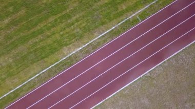 Kırmızı koşu yolunun ve yeşil çimlerin üst manzarası. Spor faaliyetleri için altyapı.