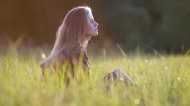 Uzun saçlı genç bir kadın yaz çimenlerinde oturmuş günbatımında doğanın tadını çıkarıyordu..