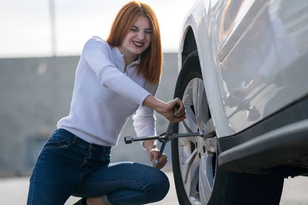 Young woman with wrench changing wheel on a broken car.