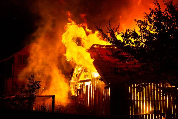 Dřevěný dům nebo stodola hoří v noci. — Stock fotografie