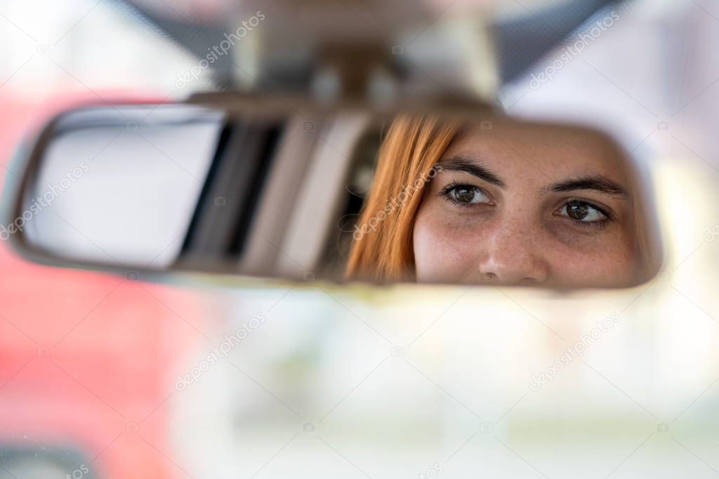 Young woman driver checking rear view mirror looking backwards w