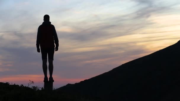dunkle Silhouette eines Wanderers, der bei Sonnenuntergang einen Berg besteigt und wie ein Sieger die Hände zum Gipfel hebt.