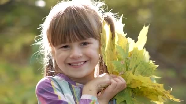 Portrait d'enfant heureuse fille avec un bouquet de feuilles d'automne jaunes souriant à la caméra sur un fond flou lumineux .