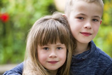 İki sevimli sarışın çocuk kardeş, erkek kardeş kız kardeşi kucaklıyor açık havada, parlak yeşil bokeh arka planda. Aile ilişkisi, arkadaşlık ve aşk kavramı.
