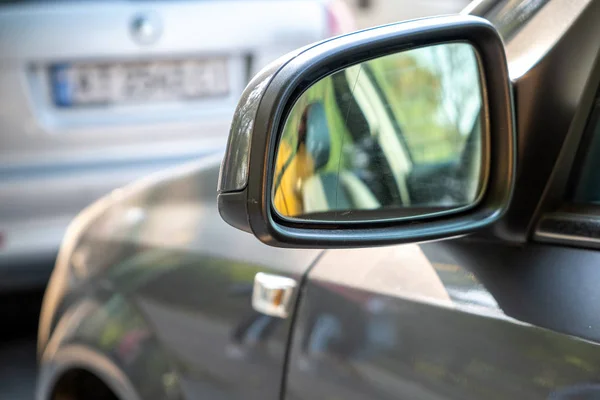 Закрыть зеркало заднего вида автомобиля, припаркованного у бордюра на обочине — стоковое фото