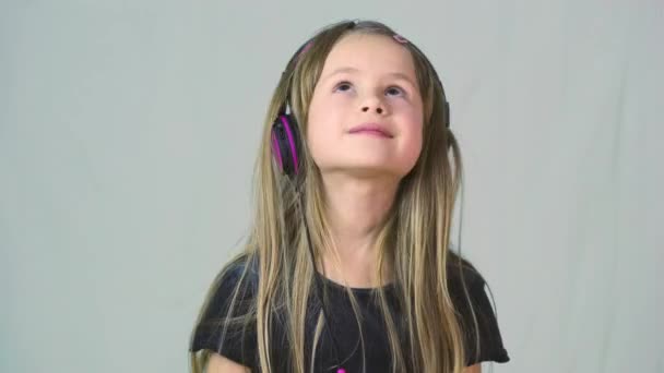 可愛いです笑顔の女の子は大きなピンクのイヤフォンで音楽を聴く — ストック動画