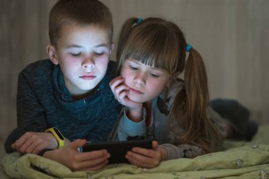 İki kız ve erkek kardeş akıllı telefondan video izliyorlar.
