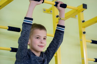 Genç bir çocuk spor dünyasının içinde, duvardaki merdiven demiri üzerinde egzersiz yapıyor.