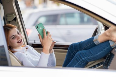 Genç kızıl saçlı kadın sürücü cep telefonuyla selfie çekiyor. 