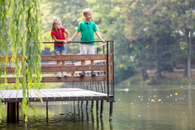 Göl kıyısında tahta güvertede duran iki kız ve erkek çocuk.