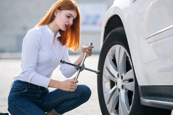 Young woman with wrench changing wheel on a broken car.