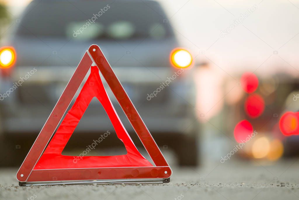 Red emergency triangle stop sign and broken car on a city street