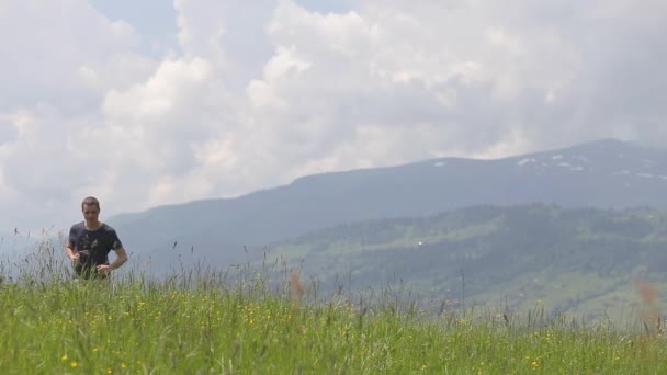夏の山の中でハイキング中に勝者のジェスチャーで手を上げる若い男の観光客 — ストック動画