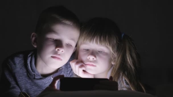 2人の子供の弟と妹は一緒にスマートフォンの画面でビデオを見て — ストック動画