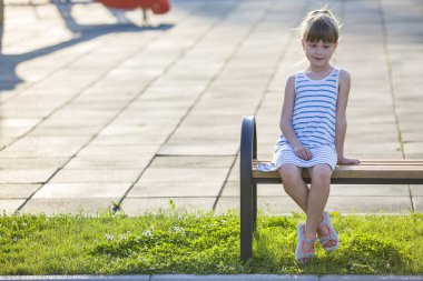 Gülücükler saçan genç kız güneşli bir yaz gününde bankta tek başına oturuyor..