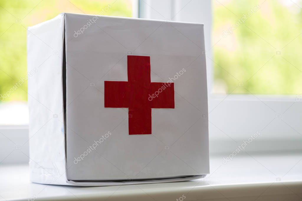 White first aid kit with red cross indoors on windowsill on blur