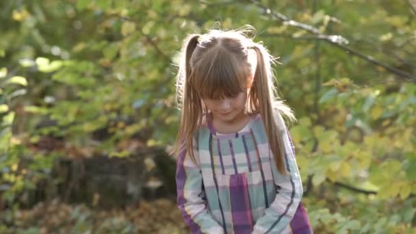 快乐的小女孩在明亮模糊的背景下把秋天的黄叶抛向空中的画像 — 图库视频影像