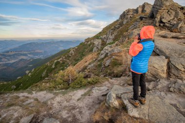 Genç çocuk dağlarda fotoğraf çekiyor. Manzaranın tadını çıkarıyor.