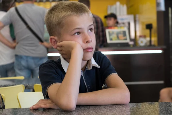 Chlapec sedí v fast food restauraci za prázdným stolem. — Stock fotografie