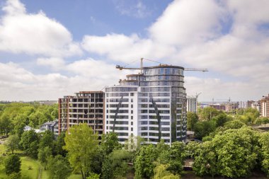 Daire veya ofis uzun boylu bina yeşil ağaç tops arasında inşaat altında tamamlanmamış. Parlak mavi gökyüzü kopya alanı arka planda kule vinçler.