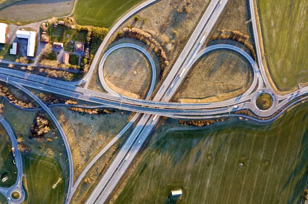 Luftaufnahme von modernen Autobahn Straßenkreuzung, Hausdächer auf frühlingshaften grünen Feld Hintergrund. Drohnenfotografie. — Stockfoto