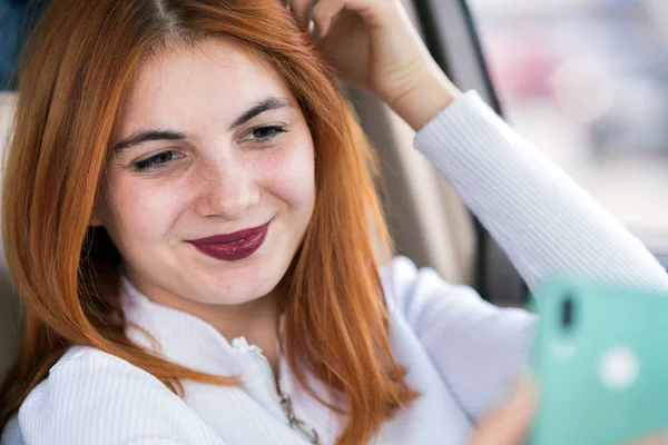 Молодая рыжая женщина водитель делает селфи с ее мобильного телефона — стоковое фото