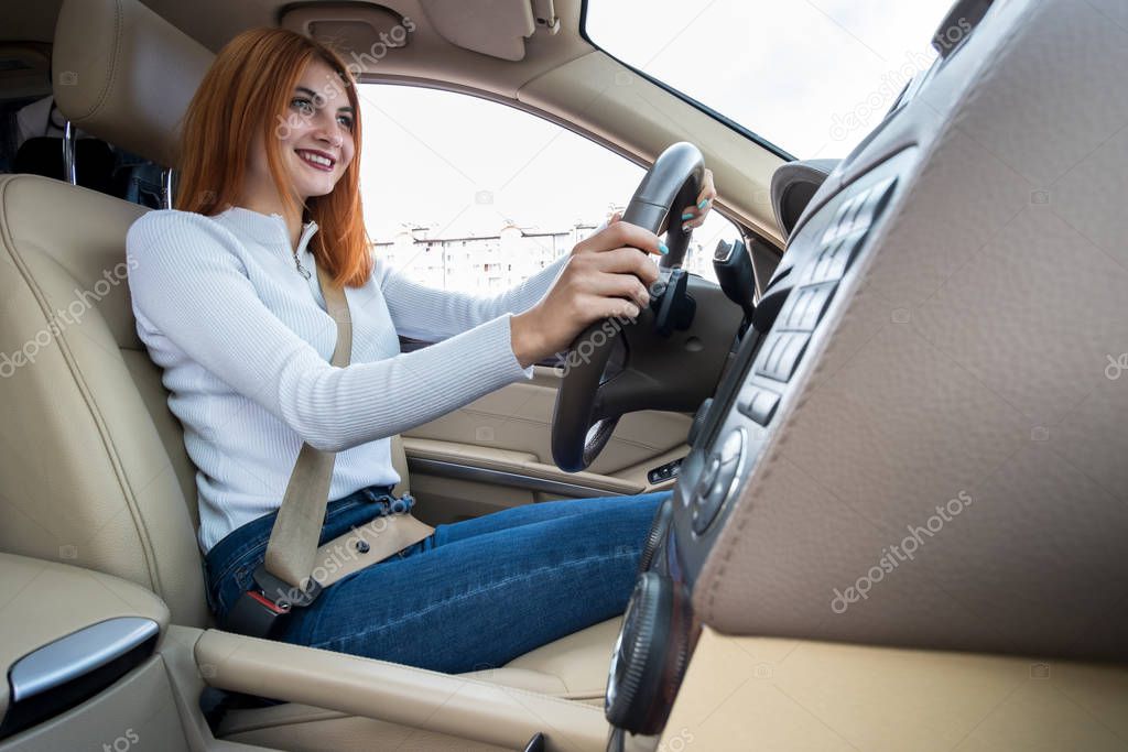 Young redhead woman driver driving a car smiling happily.