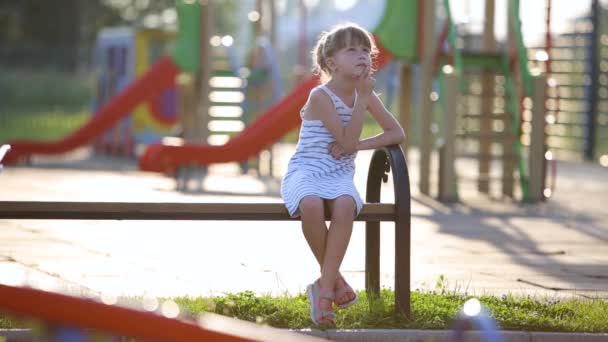 悲しい子供女の子待っていますのために彼女のお母さん座っています上のベンチ夏の遊び場で幼稚園ヤード — ストック動画