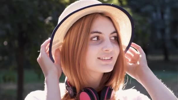 可愛いです10代の女の子のポートレートとともに赤い髪身に着けているわら帽子とピンクのイヤホン幸せなカメラ — ストック動画
