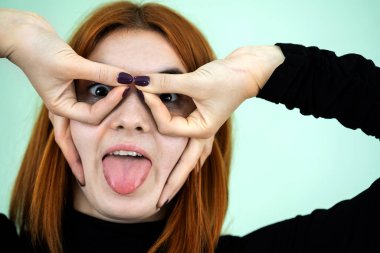 Komik kızıl saçlı kız parmaklarıyla gözlük işareti gösteriyor..