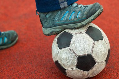 Human foot in a dirty sneaker on an old soccer ball.