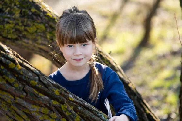 Portrait of a pretty child girl standing near a tree trunk in au — Stockfoto