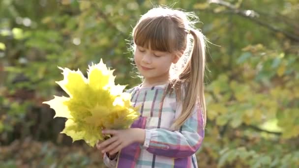 幸せな子供の女の子の肖像画とともに黄色の秋の葉笑顔でカメラで明るいぼやけた背景 — ストック動画