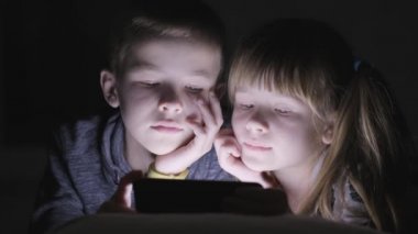 İki kız ve erkek kardeş akıllı telefondan video izliyorlar..
