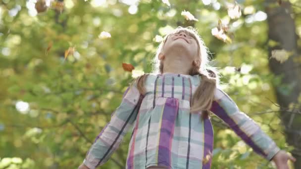 Portrait d'enfant heureuse fille avec un bouquet de feuilles d'automne jaunes souriant à la caméra sur un fond flou lumineux .
